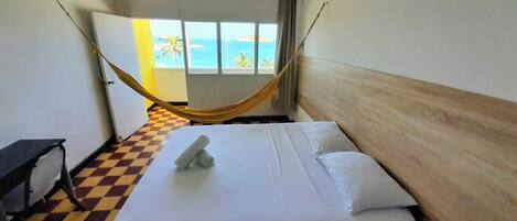 A hotel room with a bed, a checkered floor, a hammock, and a view of the ocean through a window.