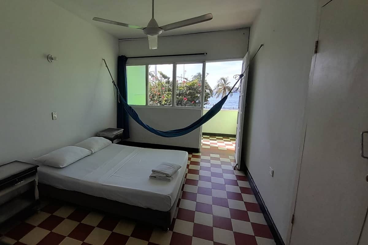 A small, clean room with a bed, a nightstand, a window with a view, and a checkered floor.
