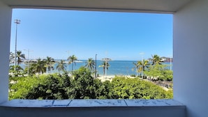 A view from a window overlooking a beach with palm trees, a clear sky, and a distant island. - panamerican hostel  (Santa Marta)
