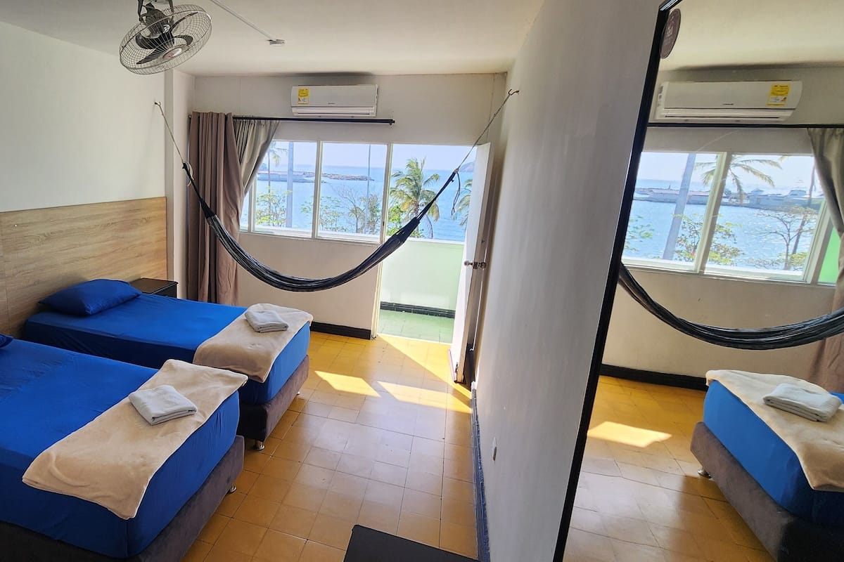 A hotel room with two beds, a hammock, and a view of the sea.