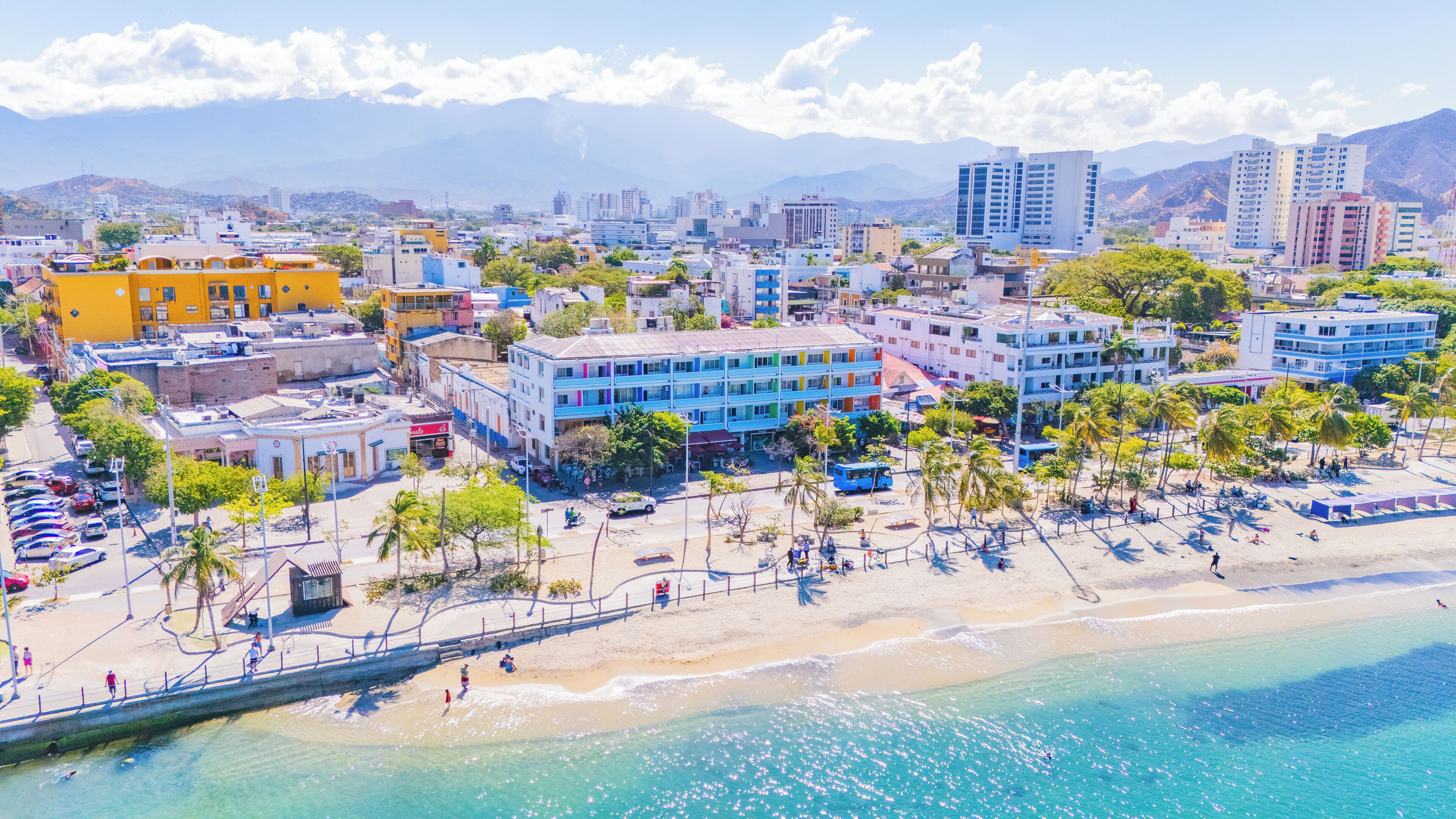 A coastal cityscape with a beach, buildings, and mountains in the background.