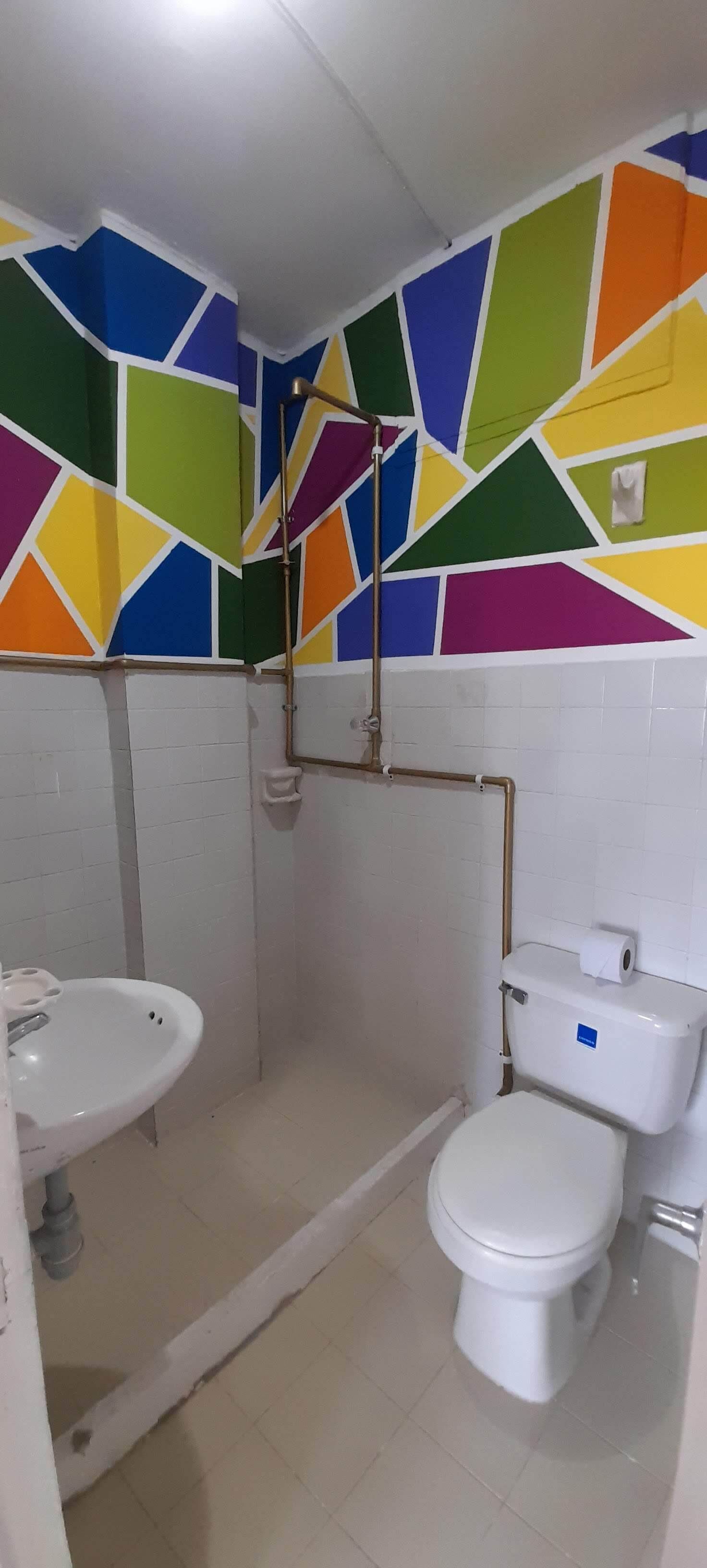 A bathroom with a white sink, toilet, and shower area. The walls are decorated with colorful geometric patterns.
