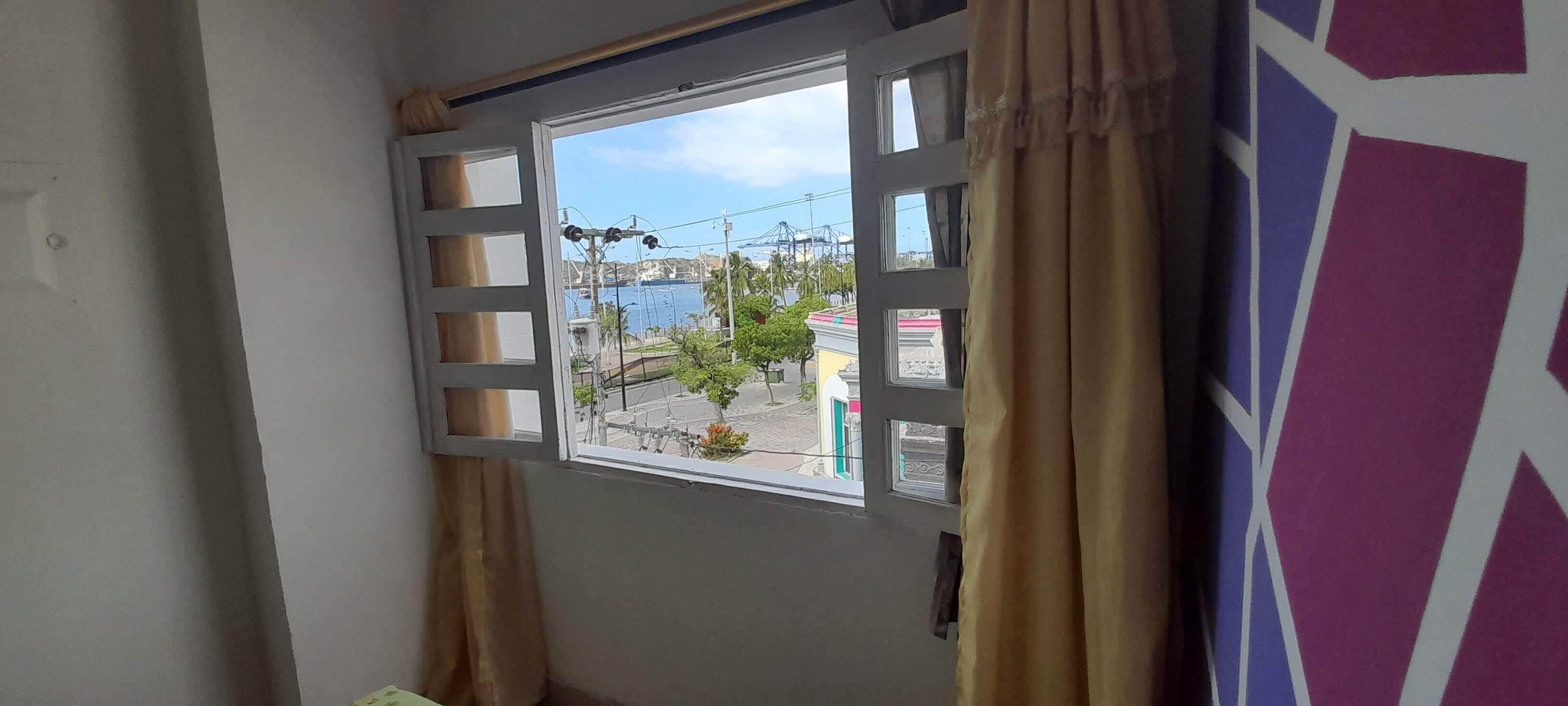 Ein Zimmer mit Fensterblick auf ein Gewässer und die Skyline, mit halb zurückgezogenem Vorhang.
