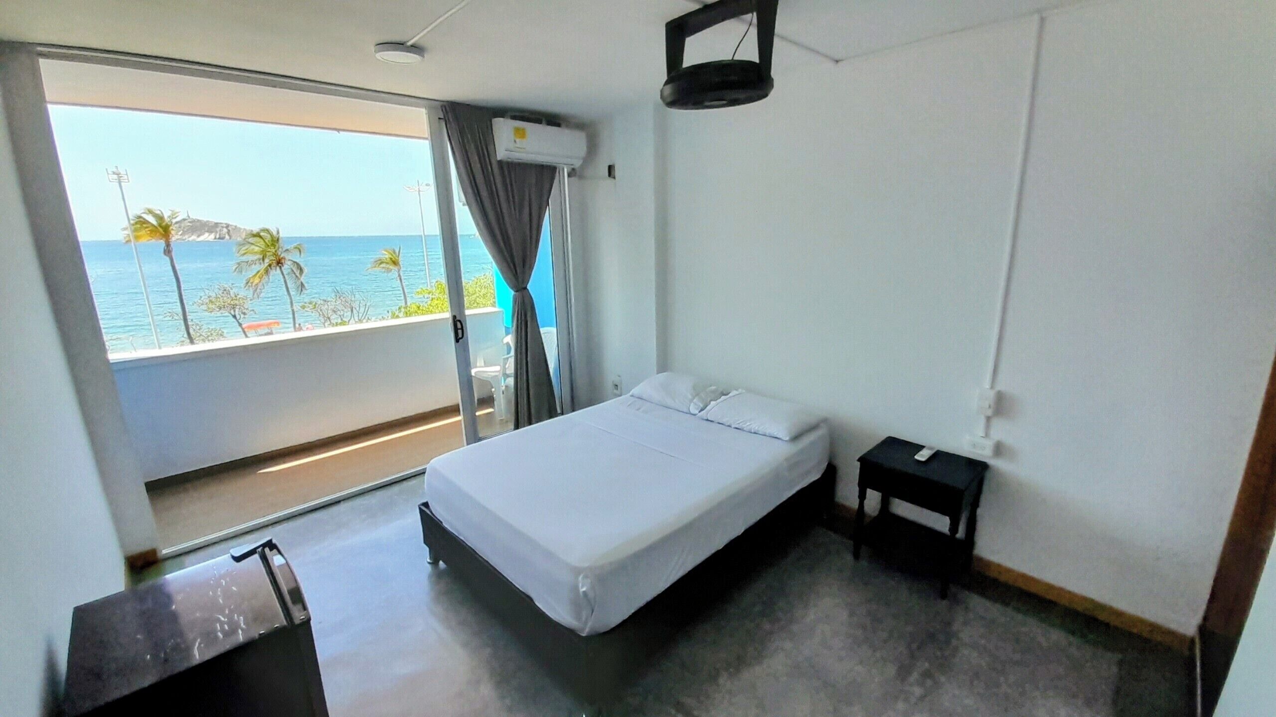 A hotel room with a bed, a small bedside table, and a view of the ocean through a balcony.