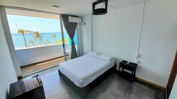 A hotel room with a bed, a small bedside table, and a view of the ocean through a balcony.
