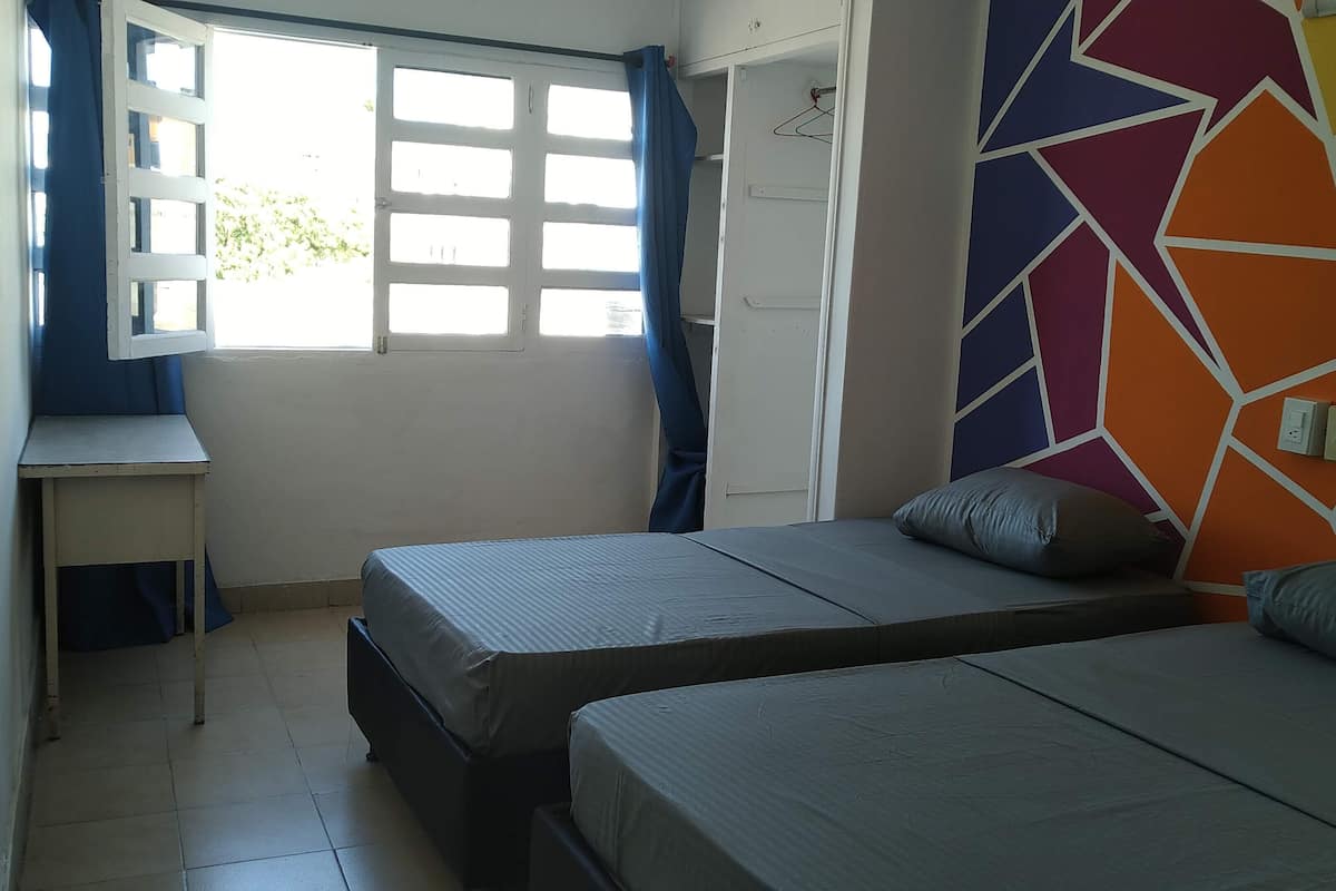 A bedroom with two beds, a desk, and a colorful geometric wall.