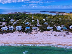 An aerial view of a coastal resort with multiple beachfront villas, a sandy beach, and a clear view of the ocean.