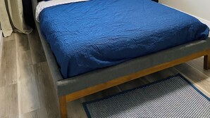 Ett sovrum med en säng, gardiner, ett fönster, en växt och ett nattduksbord.