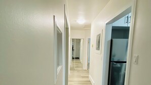 En hall med trägolv, vita väggar och ett kylskåp i bakgrunden.