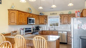 A kitchen with wooden cabinets, a granite countertop, a stainless steel refrigerator, and a window with a view.