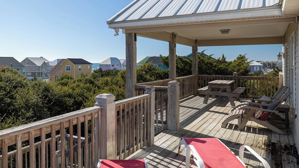 A wooden deck with a covered seating area, overlooking a residential neighborhood.