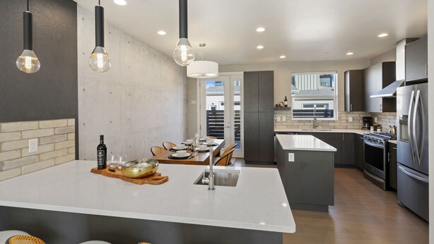 Une cuisine moderne dotée d’un îlot central, de luminaires suspendus et offrant une vue sur l’extérieur.
