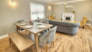 A dining area with a wooden table set for four, a grey sofa, and a fireplace. - Warm & Inviting Home | Free Parking & Wi-Fi (Lincoln)