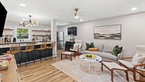 Une cuisine moderne avec un coin repas, un salon doté d’un canapé et de fauteuils, et une grande fenêtre.