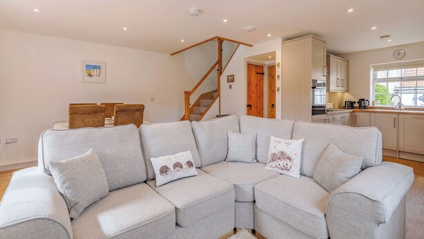 A modern living room with a sectional sofa, a staircase, and a kitchen area. - 1 bedroom accommodation in Bempton (Bempton)