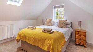 A bedroom with a sloped ceiling, a bed with a yellow blanket, two bedside lamps, a window, and a wooden nightstand. - 1 bedroom accommodation in Bempton (Bempton)