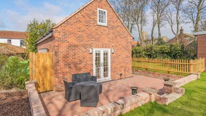 A brick house with a patio, a wooden gate, and a fenced yard. - 1 bedroom accommodation in Bempton (Bempton)