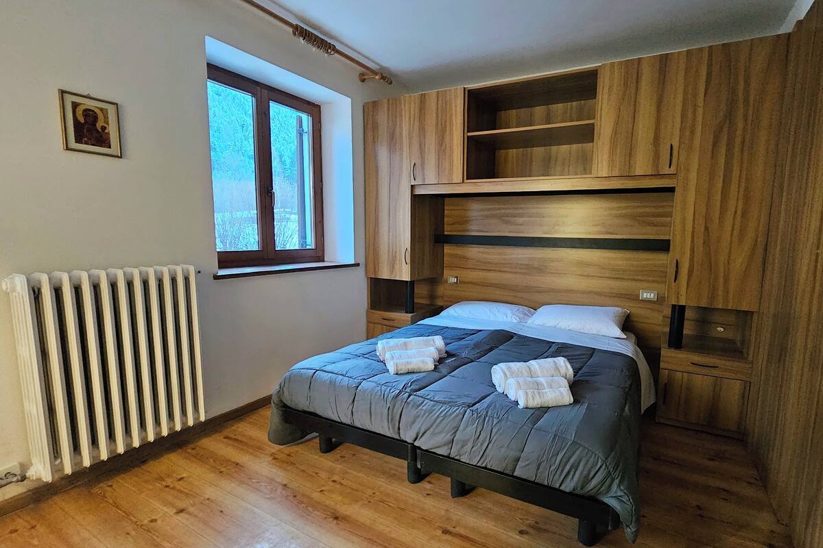 A bedroom with a wooden bed, a radiator, a window, and a picture on the wall.