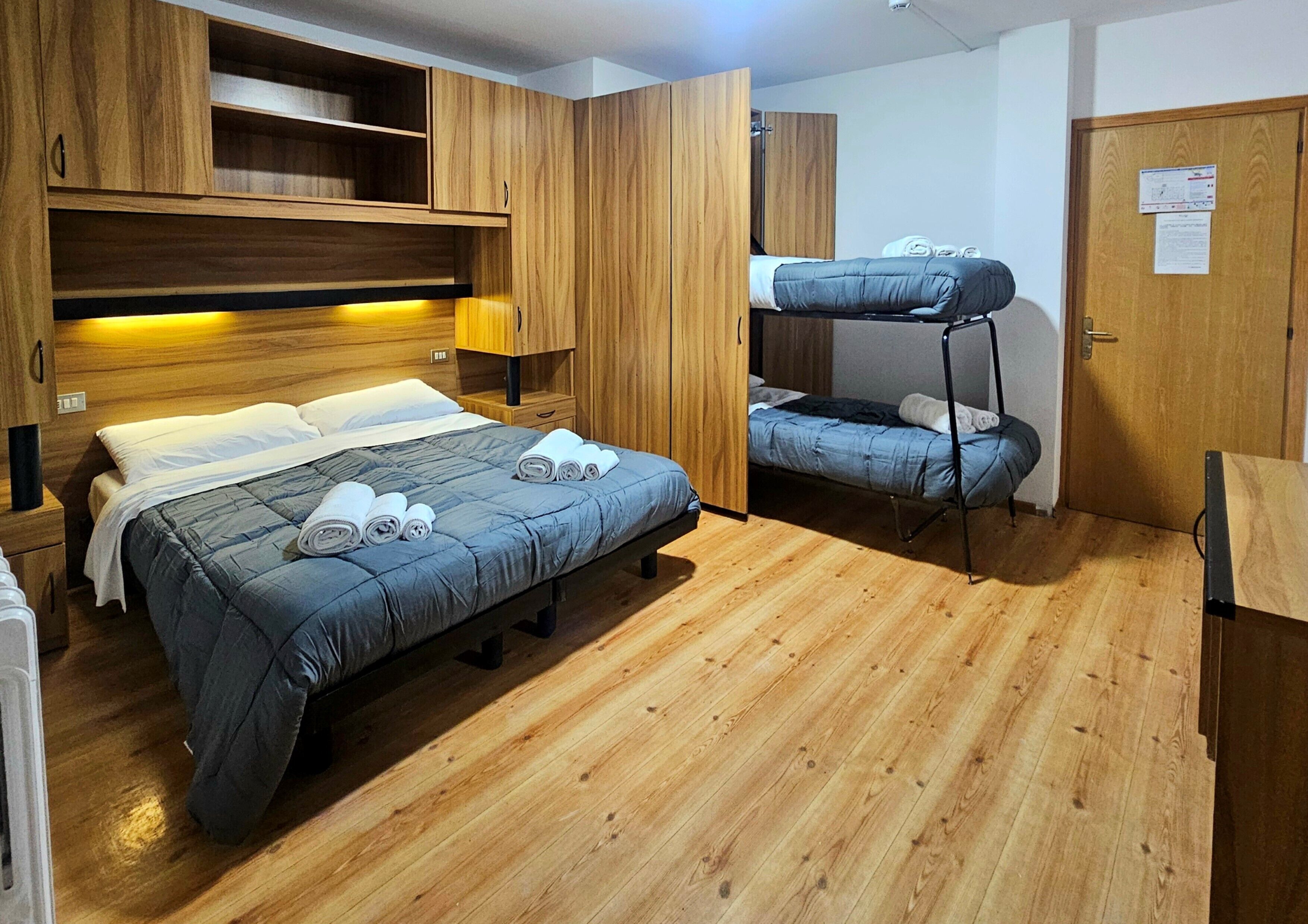 Une chambre avec un grand lit, un plus petit lit, des armoires en bois et un bureau.