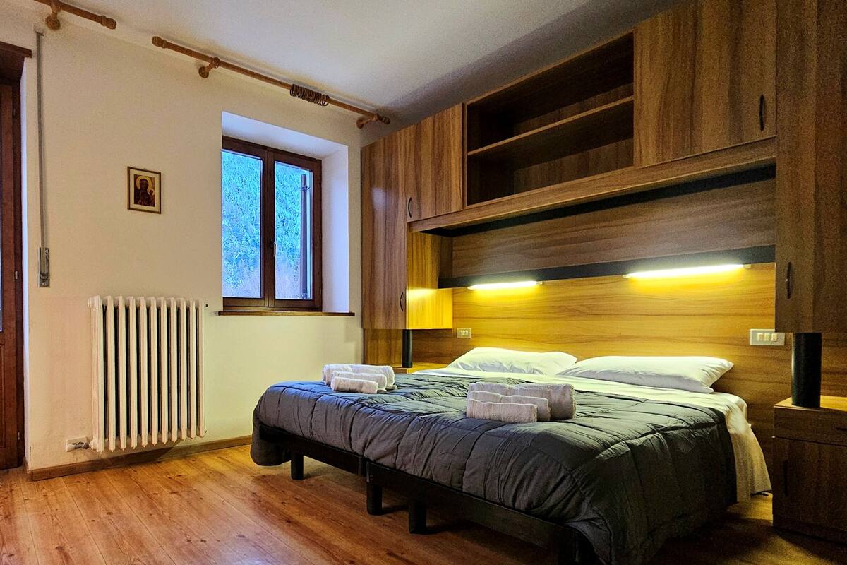 A bedroom with a bed, wooden headboard, window, radiator, and a small picture on the wall.