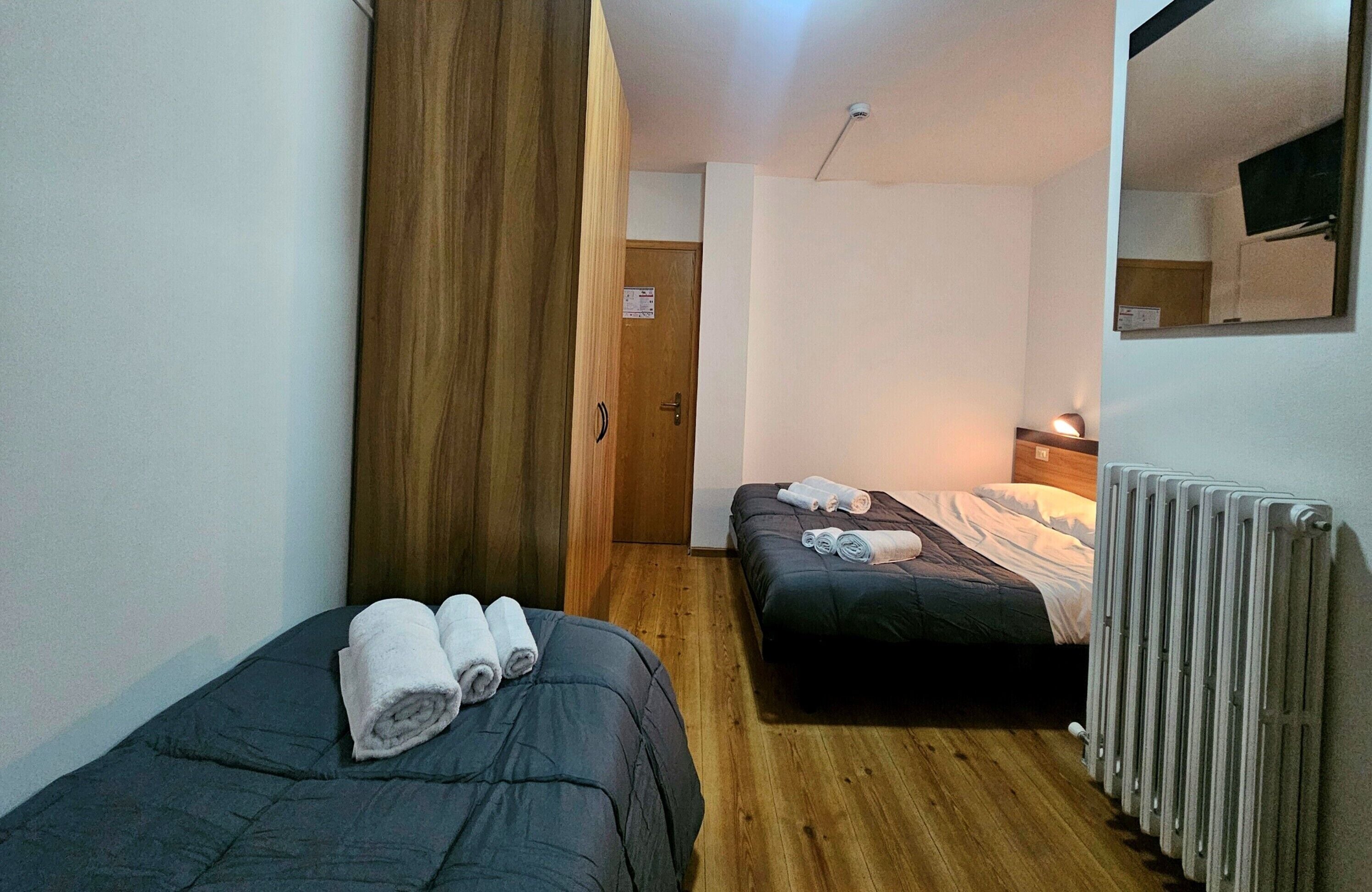 A small, compact room with two single beds, wooden flooring, a radiator, and a mirror on the wall.