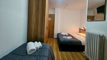 Una habitación pequeña y funcional con dos camas individuales, suelo de madera, un radiador y un espejo en la pared.
