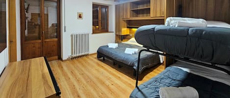A dormitory room with bunk beds, a wooden desk, a radiator, and a window.