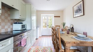 A kitchen with white cabinets, a microwave, and a tiled floor. There is a dining table with chairs and a colorful rug.