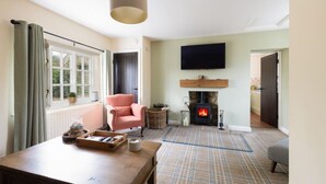 A cozy living room with a fireplace, a television mounted above it, and a comfortable seating area with a table and a chair.