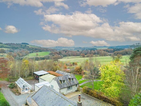 A rural house with a large garden, a greenhouse, and a view of rolling hills.