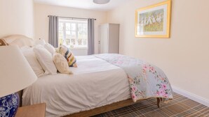 A neatly made bed with a floral duvet, a bedside lamp, and a plaid rug on the floor.