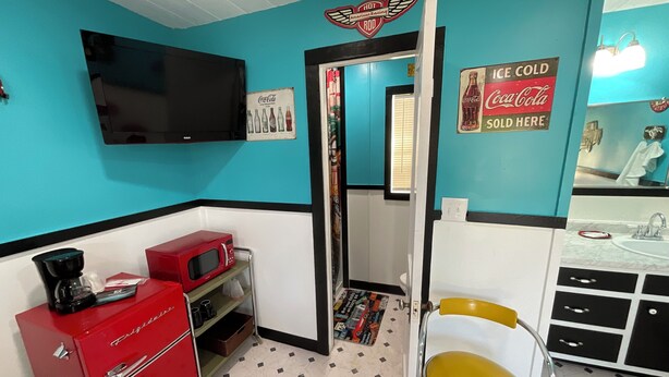 A retro-themed room with teal walls, a red appliance, a yellow chair, and a television mounted on the wall. - Cozy cabin in soothing Thackerville with AC, WiFi 1 mile and 1/4 from WINN STAR. (Thackerville)
