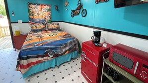 A bedroom with a bed featuring a colorful car-themed bedspread, a red dresser, a red coffee maker, and a television mounted on the wall. - Cozy cabin in soothing Thackerville with AC, WiFi 1 mile and 1/4 from WINN STAR. (Thackerville)
