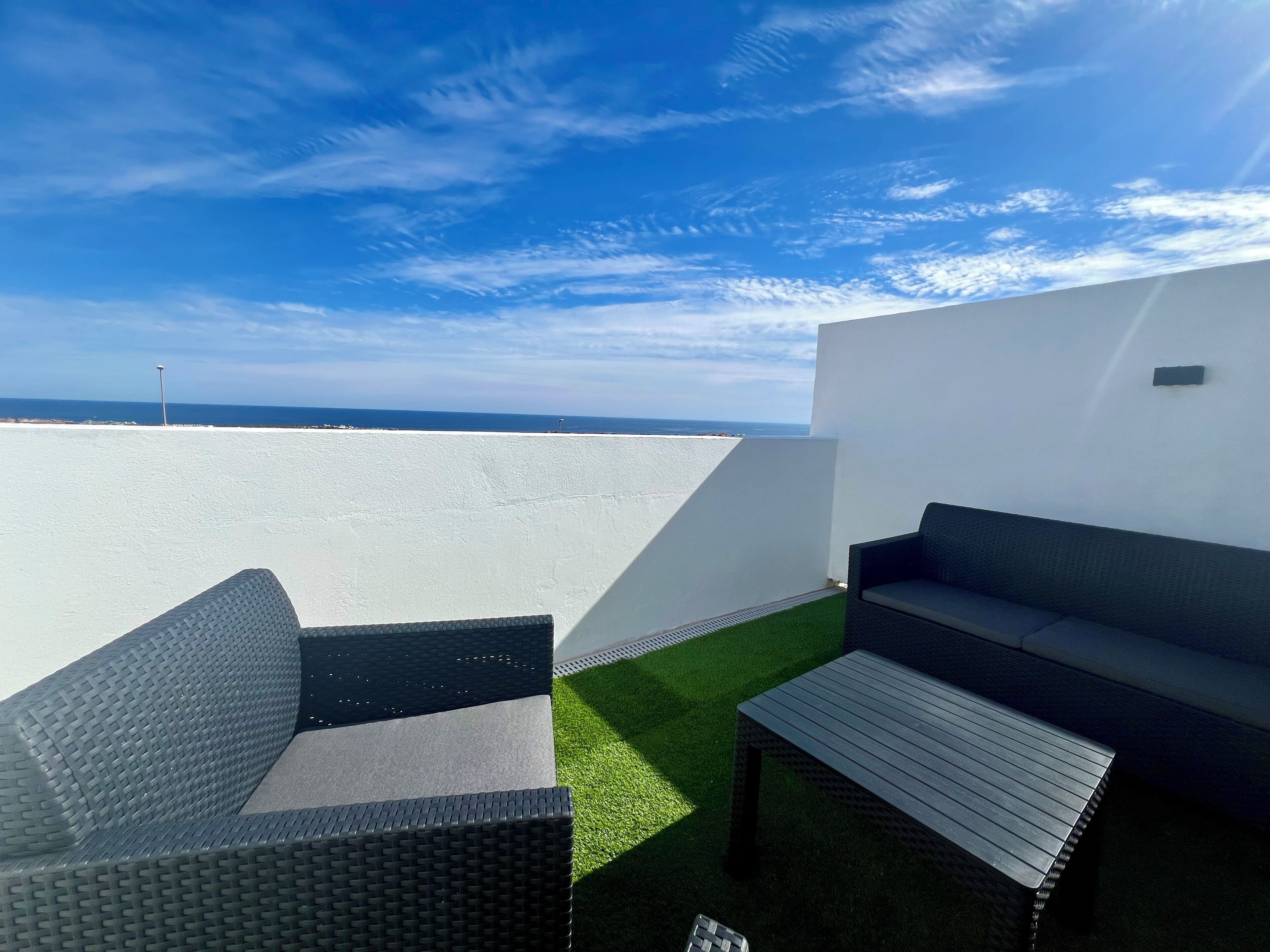 A rooftop terrace with two wicker sofas, a small table, and a view of the ocean.