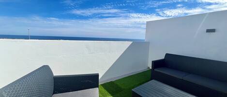 A rooftop terrace with two wicker sofas, a small table, and a view of the ocean.
