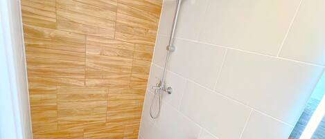 A modern bathroom with a wooden floor, white tiles, a white toilet, a shower with a handheld showerhead, and a small sink with a wooden countertop.