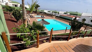 Ein Poolbereich mit freiem Blick auf den Pool, umgeben von Palmen und Kakteen, mit einer gefliesten Terrasse, die zum Pool führt.