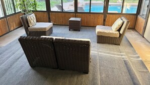 Ein Wintergarten mit Korbmöbeln, Blick auf einen Hinterhof mit Pool und Holzvertäfelung.