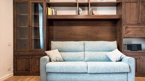 Un sofá azul claro con dos almohadones en una habitación con suelo de madera y estanterías empotradas de madera con libros y objetos decorativos.