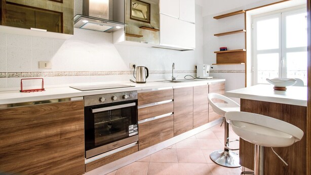 Una cocina moderna con horno integrado, cafetera y taburetes de bar.