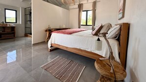 A spacious bedroom with a large bed, a wooden headboard, a woven hanging light, and a view of the outdoors through a window. - Villa Serenity (Saint martin)
