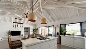 A modern kitchen with a central island, white cabinetry, and a ceiling with exposed beams. - Villa Serenity (Saint martin)