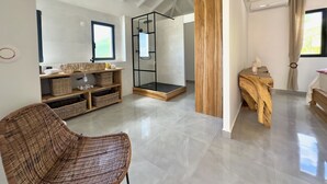 A modern bathroom with a glass shower enclosure, a wooden vanity, and a wicker chair. - Villa Serenity (Saint martin)