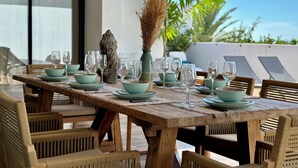 A dining table set with teal bowls and wine glasses, surrounded by wicker chairs, with a decorative vase and a stone sculpture on the table. - Villa Serenity (Saint martin)