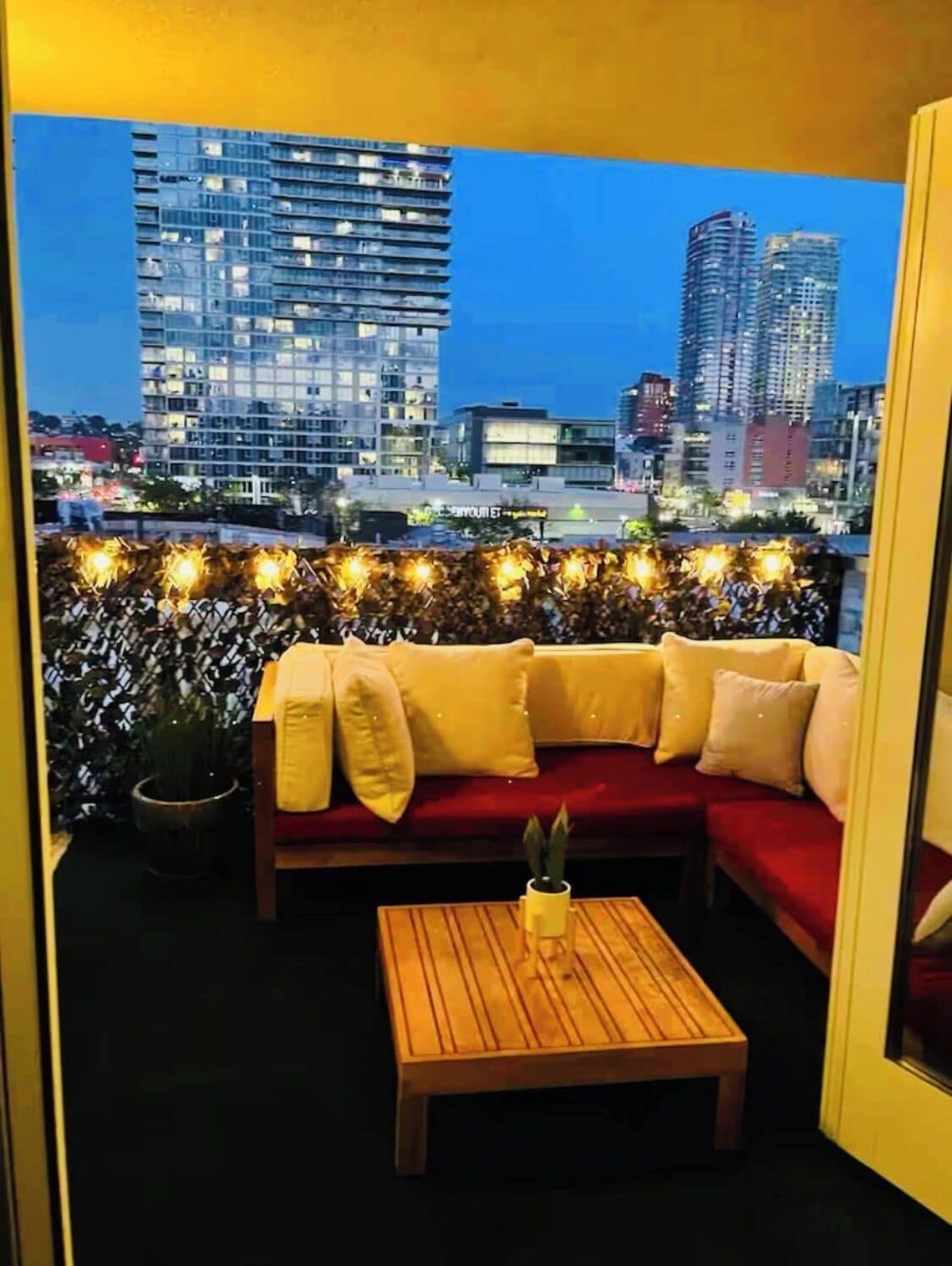 A balcony with a red sofa, a wooden table, and string lights.