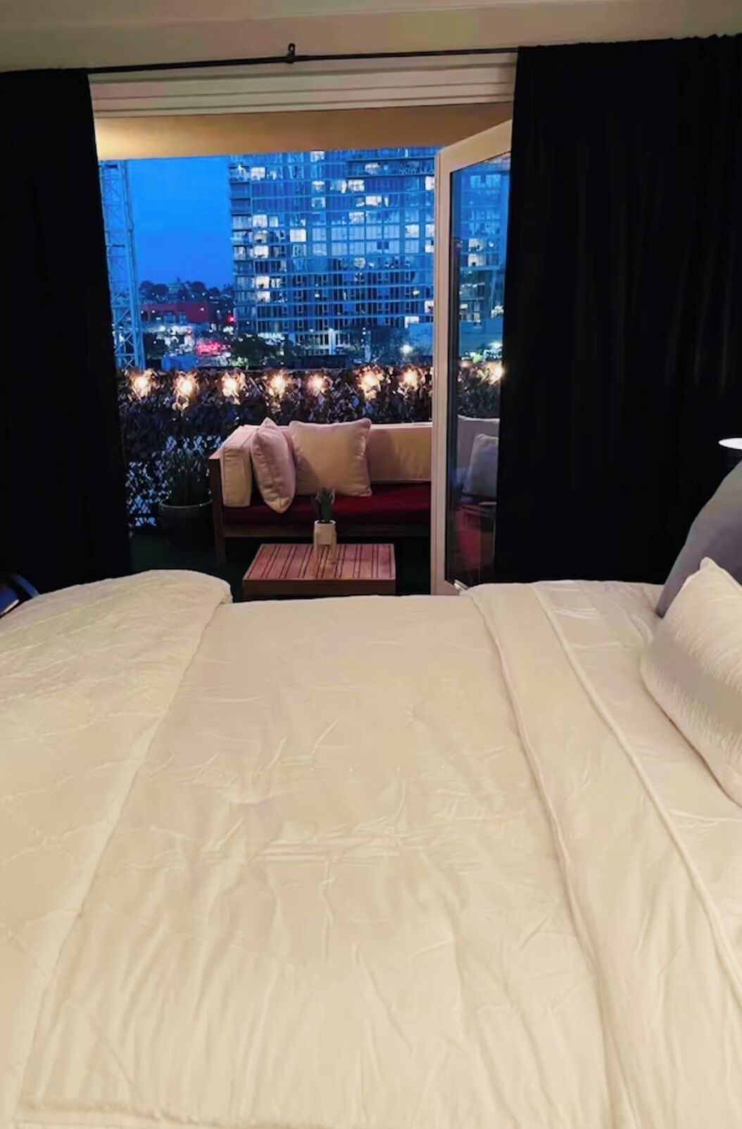A hotel room with a large bed, a sofa with cushions, and a view of a cityscape at night.