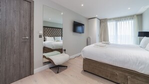 A modern hotel room with a large bed, a TV mounted on the wall, and a mirror reflecting the room. - Stylish Three-Bedroom Battersea Flat (London)