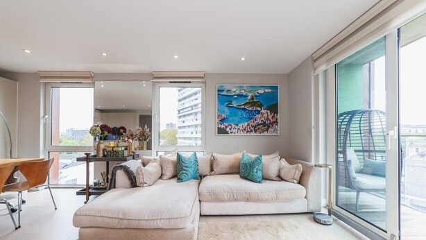 A modern living room with a sectional sofa, a dining area, and a large window with a city view. - Stylish Three-Bedroom Battersea Flat (London)