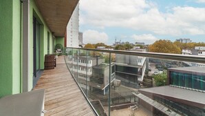 A balcony with a view of a cityscape, a wooden floor, and a glass railing. - Stylish Three-Bedroom Battersea Flat (London)