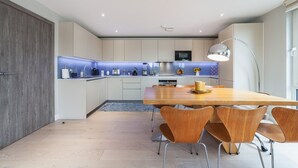 A modern kitchen with a central island, white cabinets, and a dining area with wooden chairs and a table. - Stylish Three-Bedroom Battersea Flat (London)